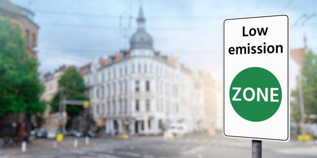 a city view with a road and a building in the background and at the front on the right a sign with written on it Low emission zone