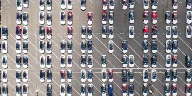 Aerial view of a car storage park where many cars are the same model. Most are white with sunroofs