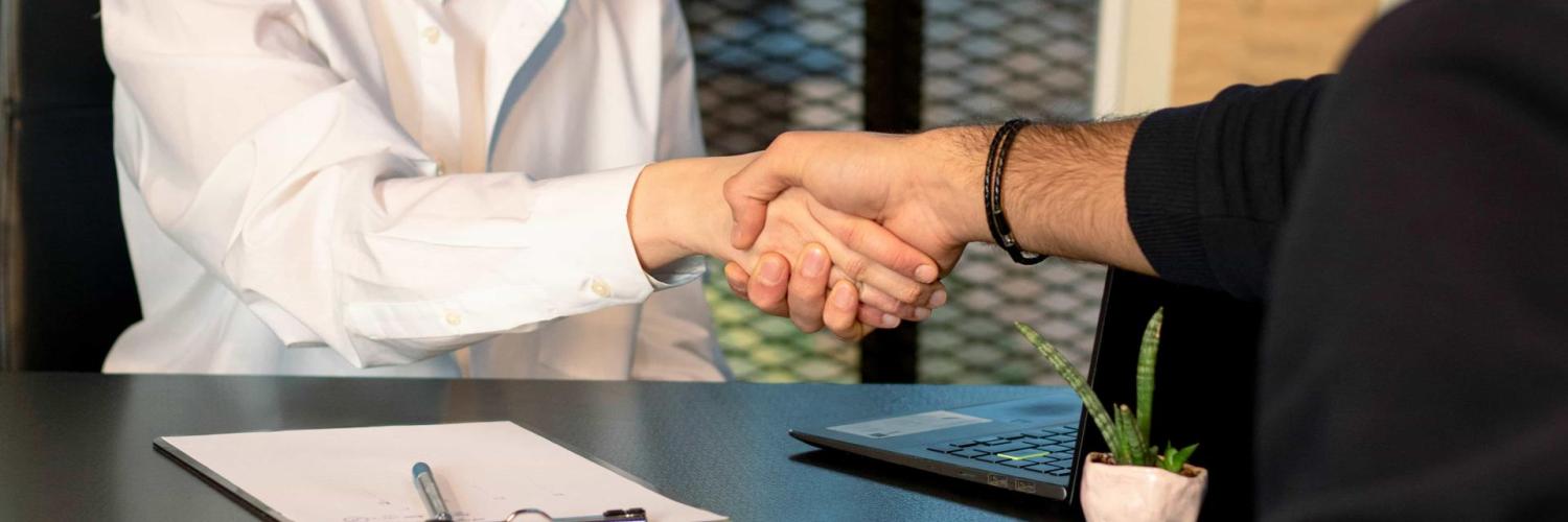 Two people shaking hands sitting on each side of a desk