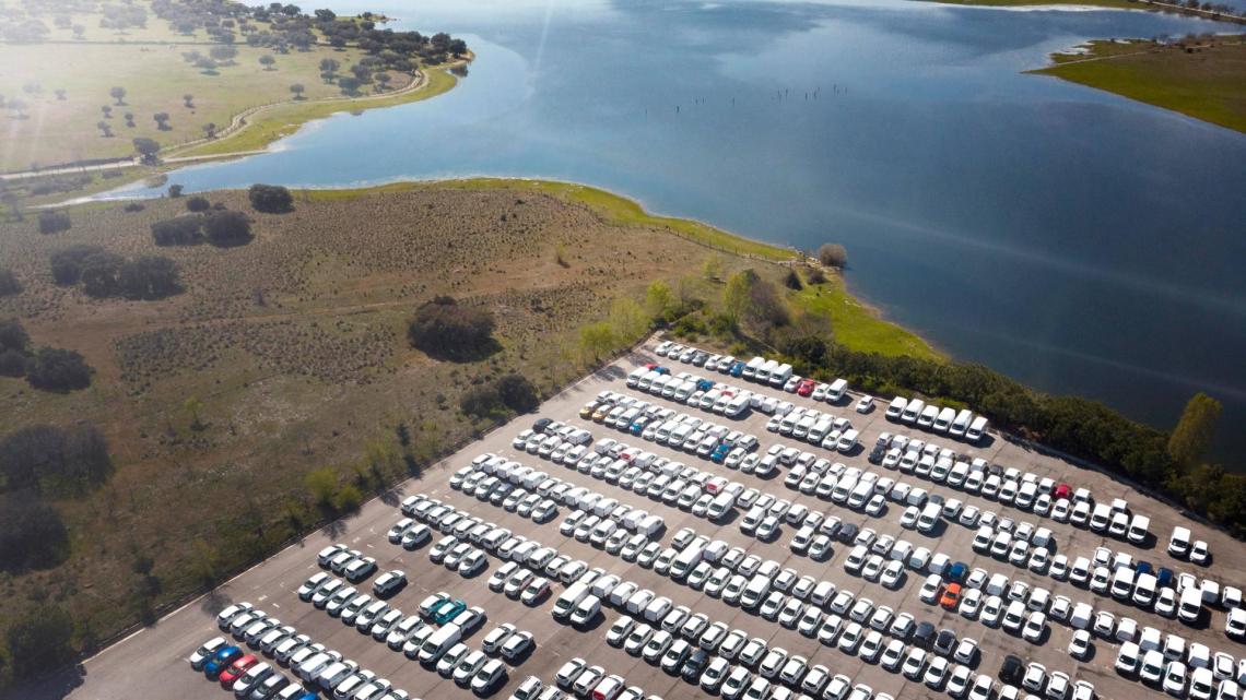 a birds eye view of a storage park with vehicles parket. Further away you can see the sea and some land with grass